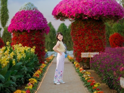 Woman stands in a lavish outdoor flower garden with mounds of colorful flowers and mushroom-like structures.