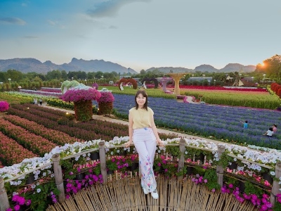 Woman stands inside a unique floral structure high above a lavish outdoor garden with mounds of colorful flowers.