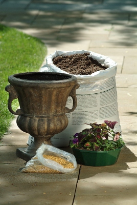 Outdoor patio with a decorative planter, bag of soil, bag of fertilizer and an assortment of flowers ready to be planted
