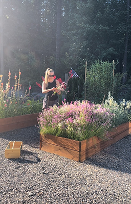Woman with flowers standing outside among raised garden beds
