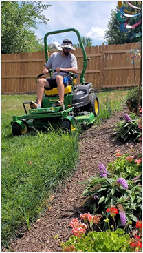 A man on a riding mower next to a flower bed