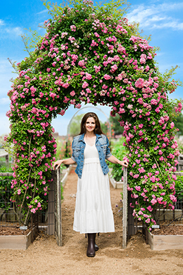 A woman standing under an outdoor flower arch filled with pink blooms