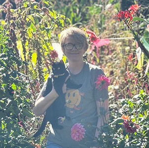 Smiling woman holding a black cat in a garden